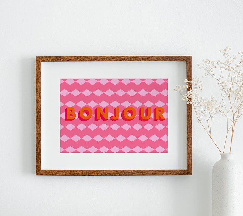 A colourful framed print featuring a geometric background and the words "bonjour" hanging on a white wall