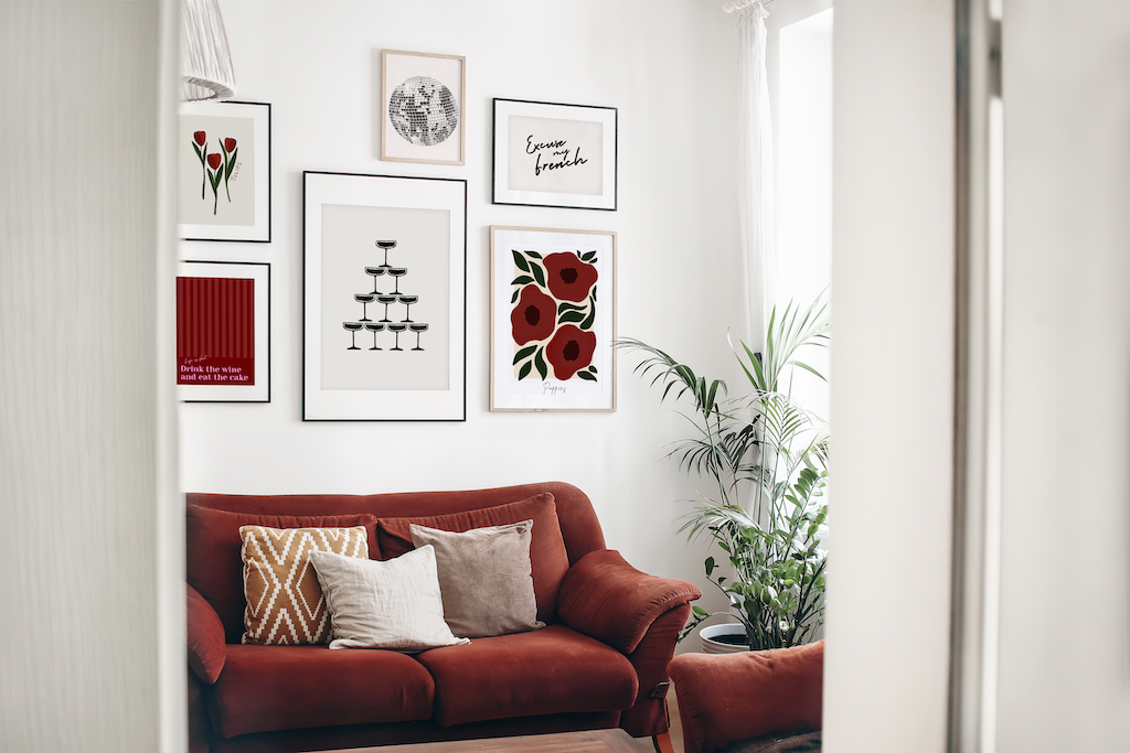 A gallery wall featuring various prints and posters above a red sofa and plant