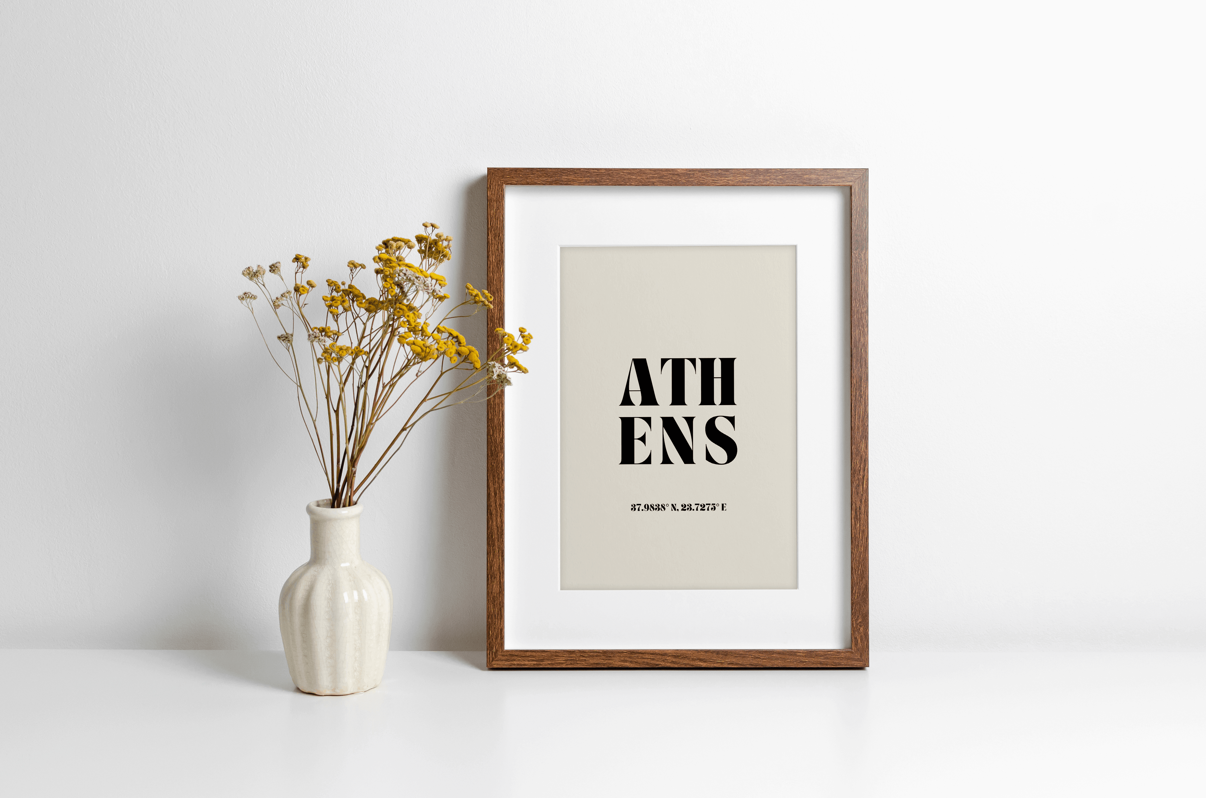 "Athens" typography print featuring coordinates, displayed in a wall leaning frame in a room with neutral decor.
