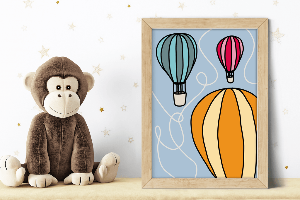 A art print featuring an illustration of hot air balloons in red, orange and green, against a blue background. Displayed in a wooden frame alongside a plush monkey toy