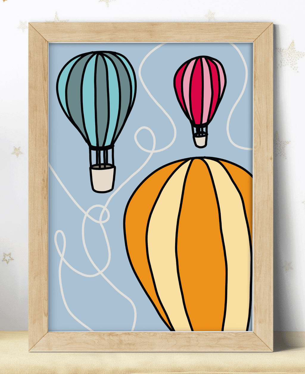 A colourful poster featuring orange, green and red hot air balloon illustration, displayed in a wooden frame.
