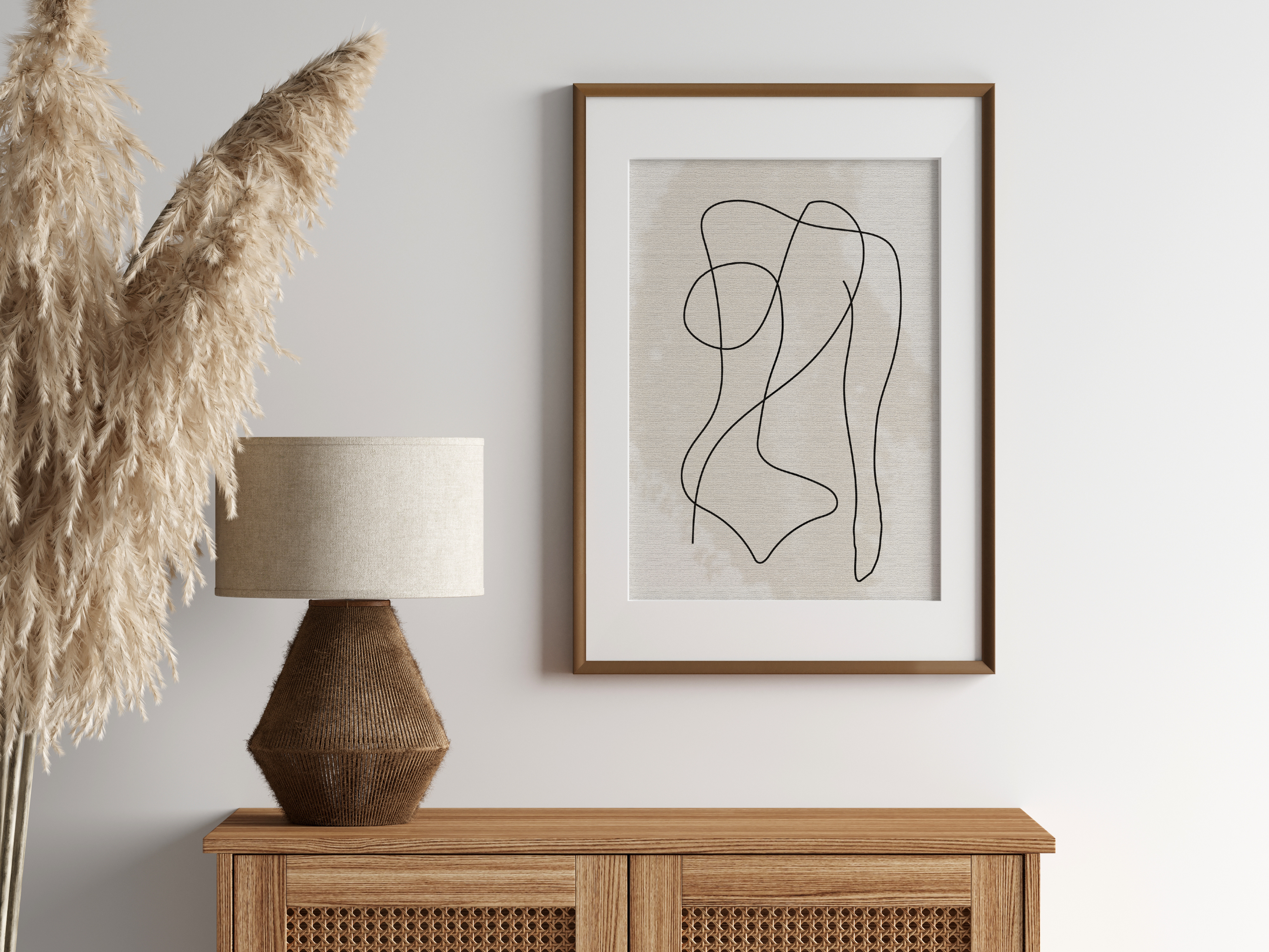 Minimalist line art print featuring a line drawing of female body, on a neutral background displayed in a wall hung wooden frame above sideboard with lamp and decorative pampas.