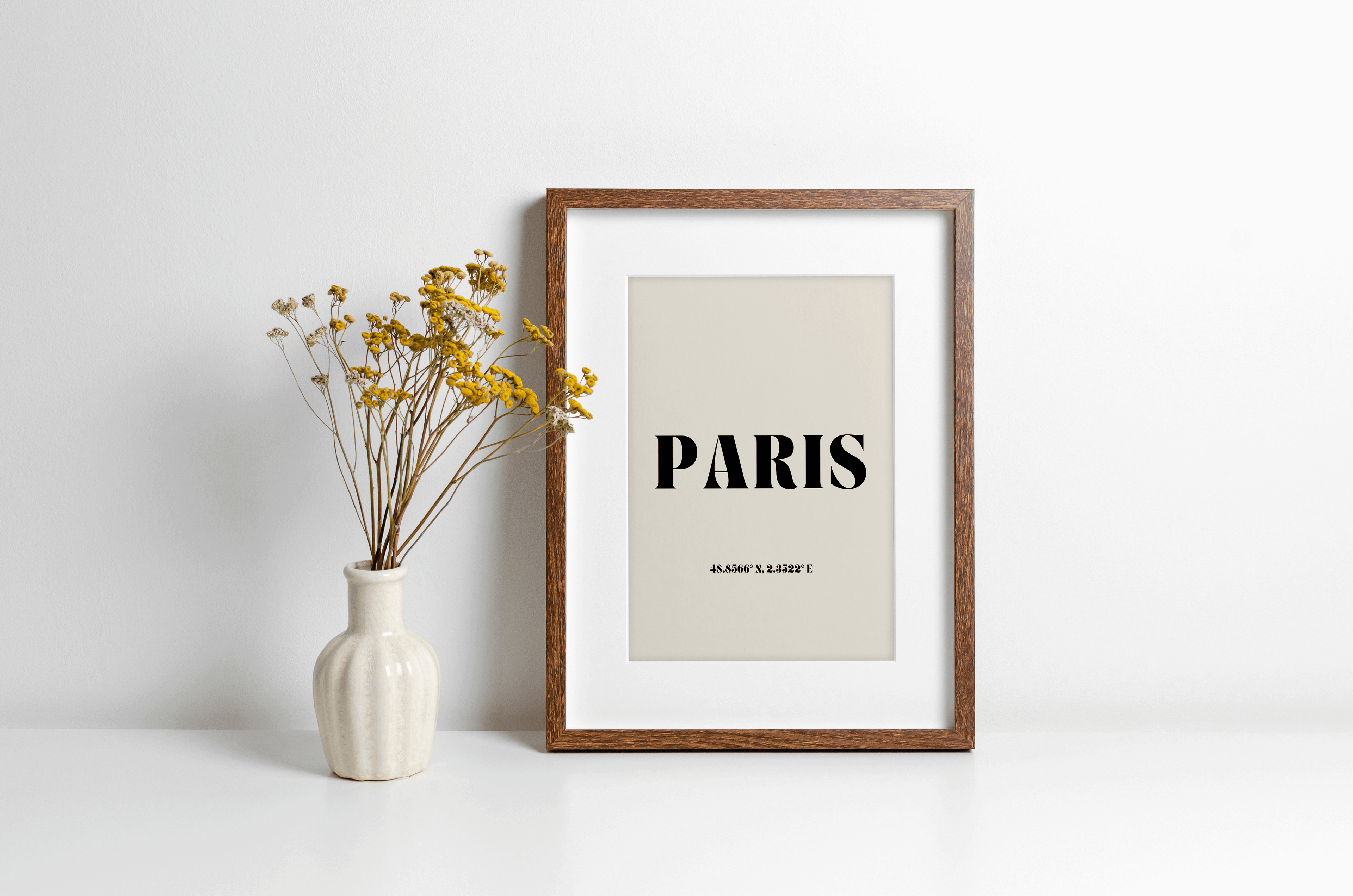 "Paris" typography print featuring coordinates, displayed in a wall leaning frame in a room with neutral decor.