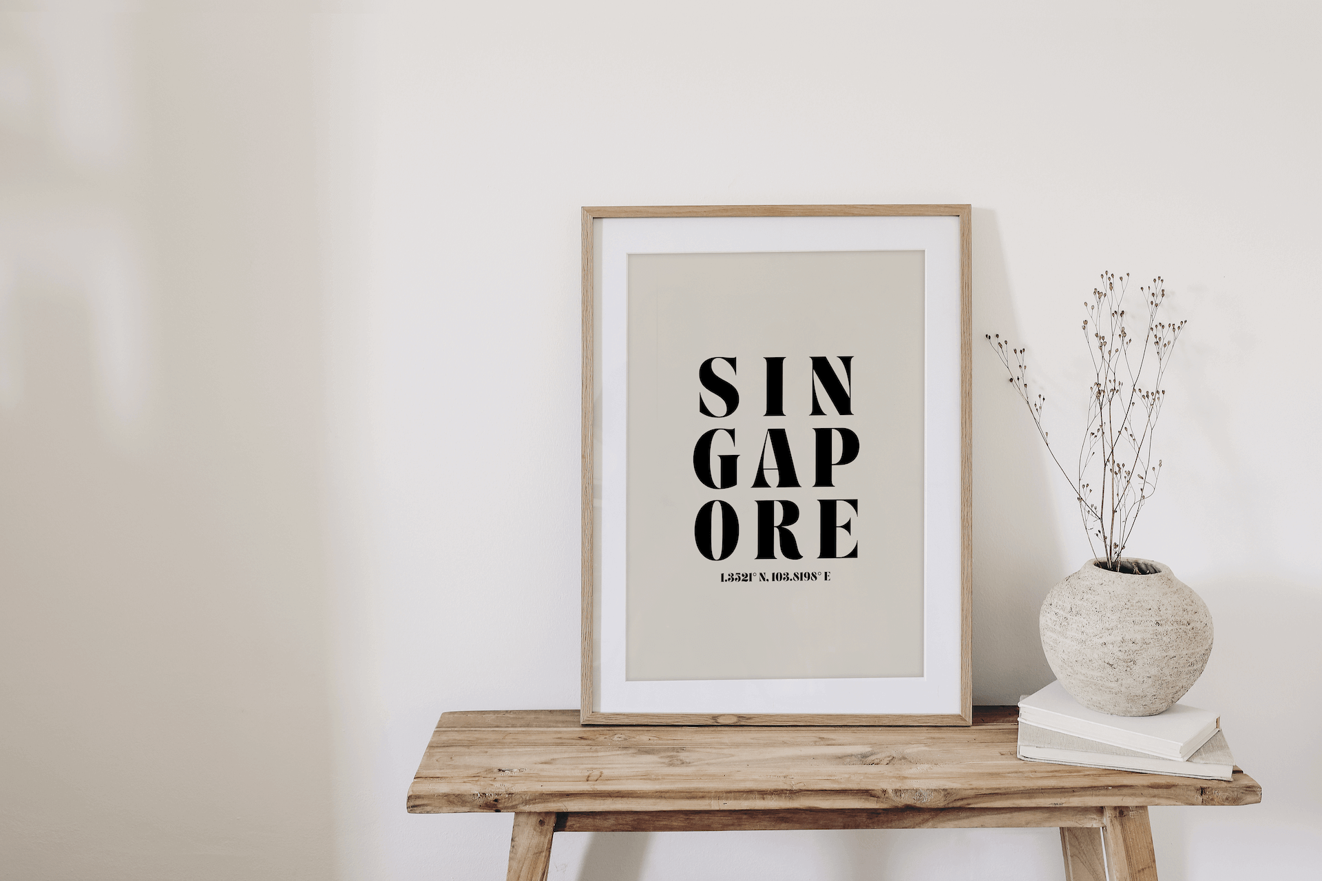 "Singapore" typography print featuring coordinates, displayed in a wall leaning frame on a bench in a room with neutral decor.