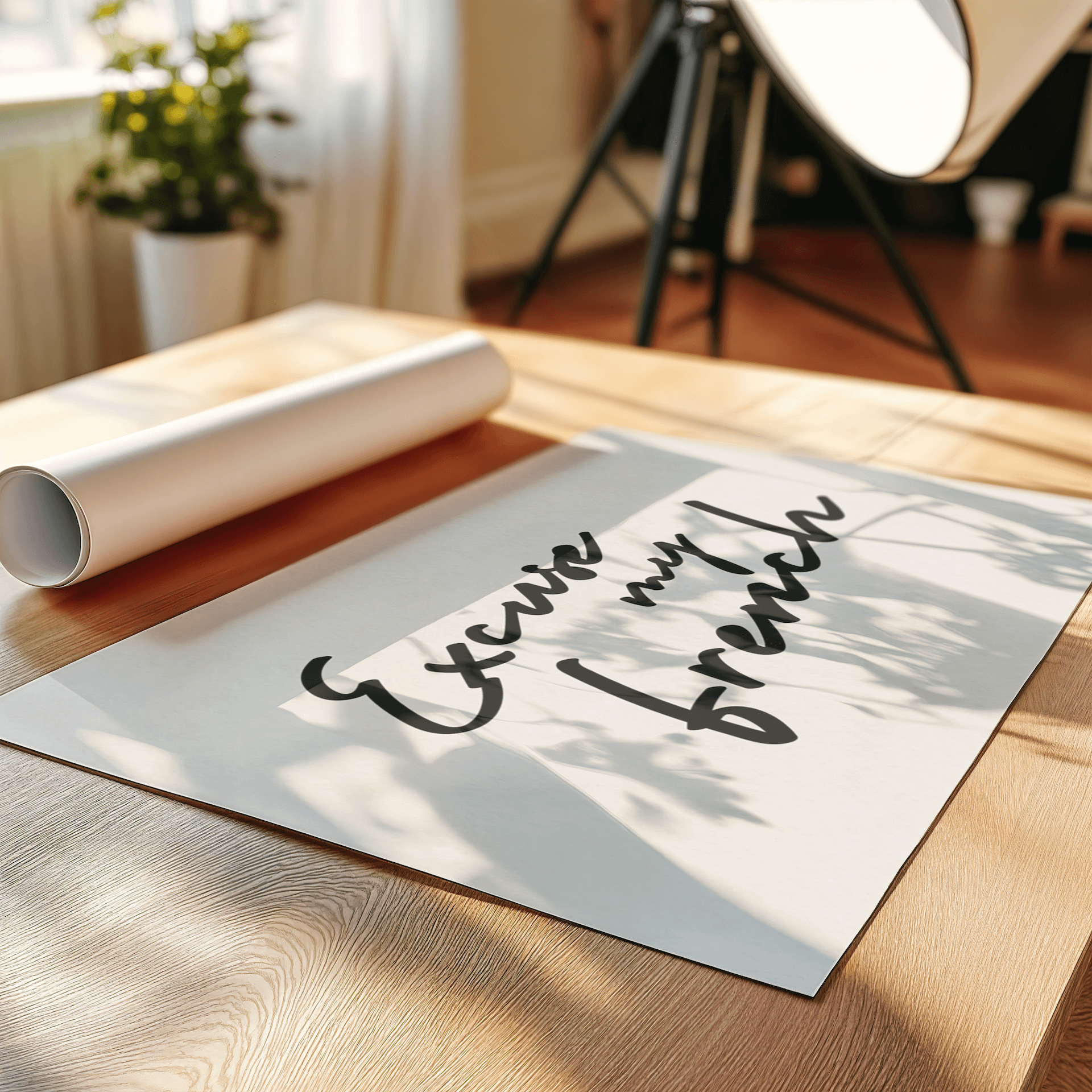 An art print laying on a table with typography "Excuse my French" surrounded by decorative plant and lamp