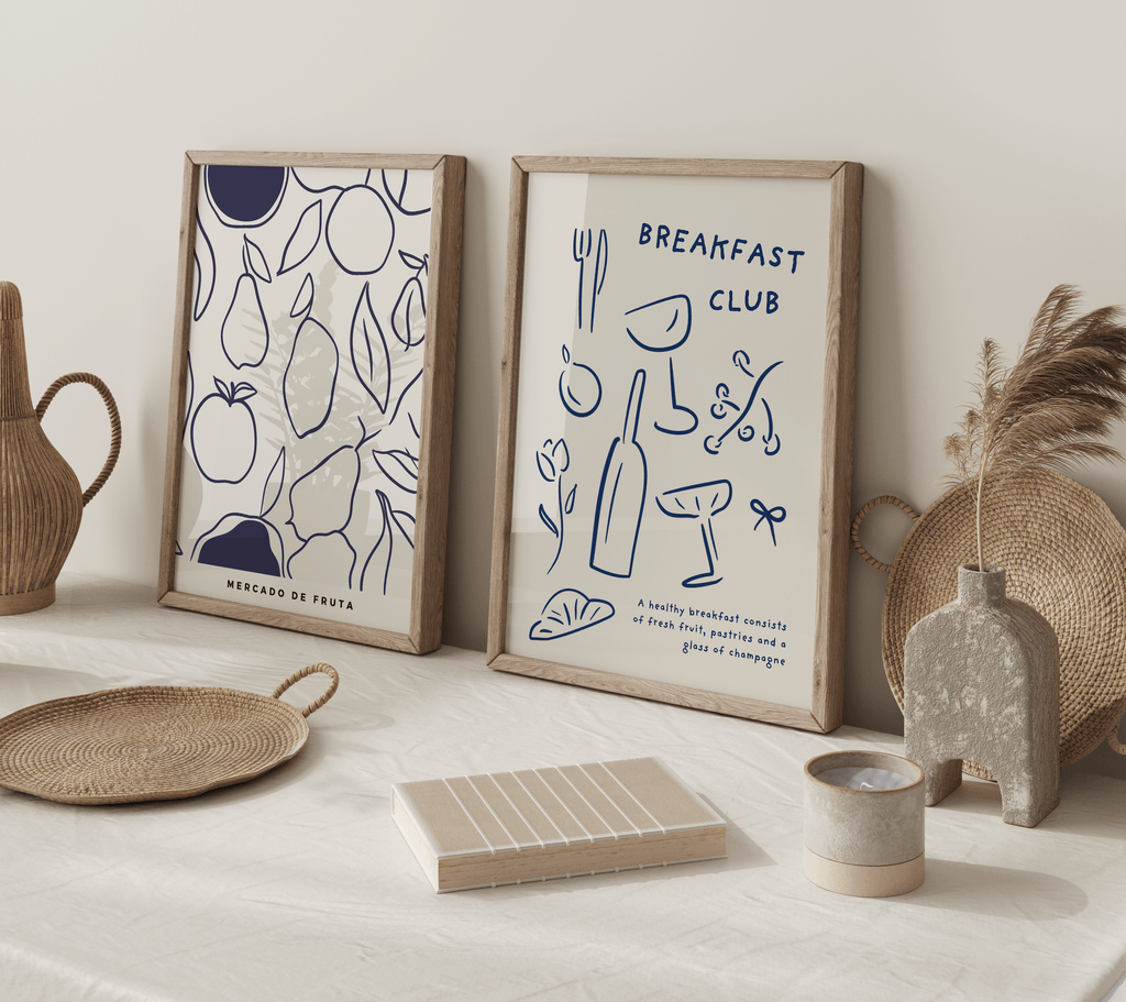 Two framed kitchen prints "breakfast club" and "mercado de fruta (fruit market)" on a counter top with decorative items