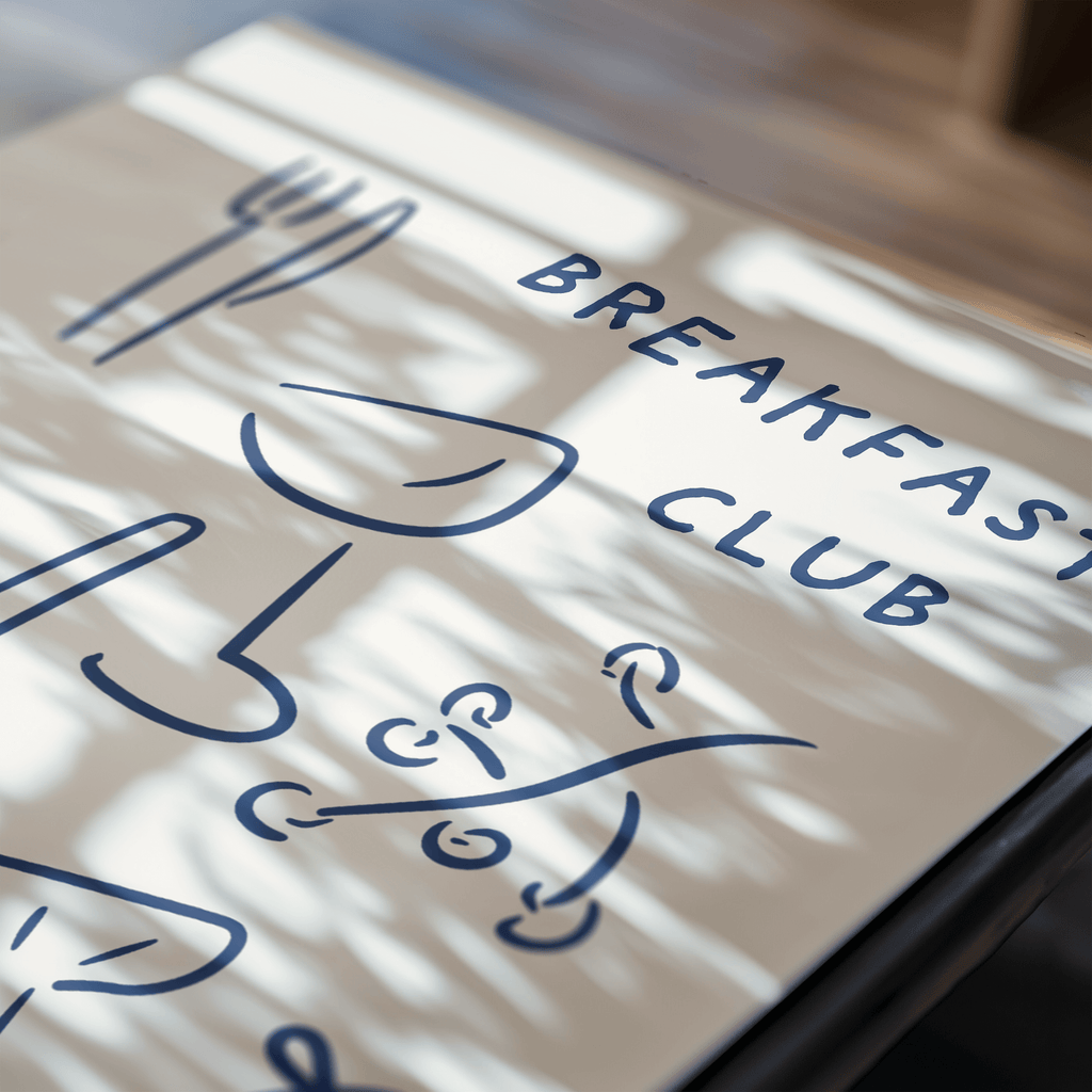 Art print displaying 'Breakfast Club' with decorative text on a light surface.