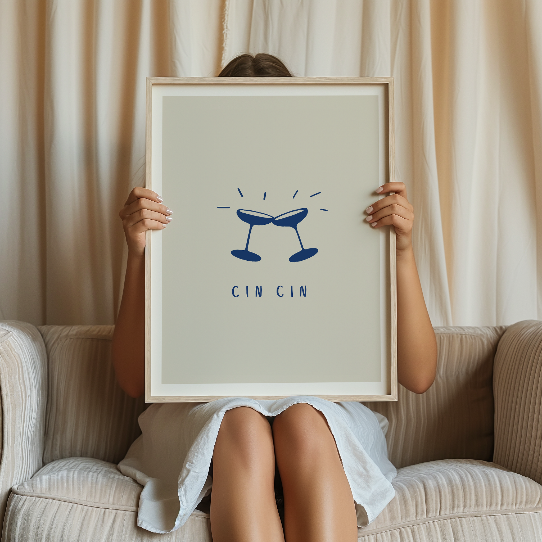 Person holding a framed art print featuring an illustration of two wine glasses clinking together and Italian typography "Cin Cin". The design has a beige background and white border.