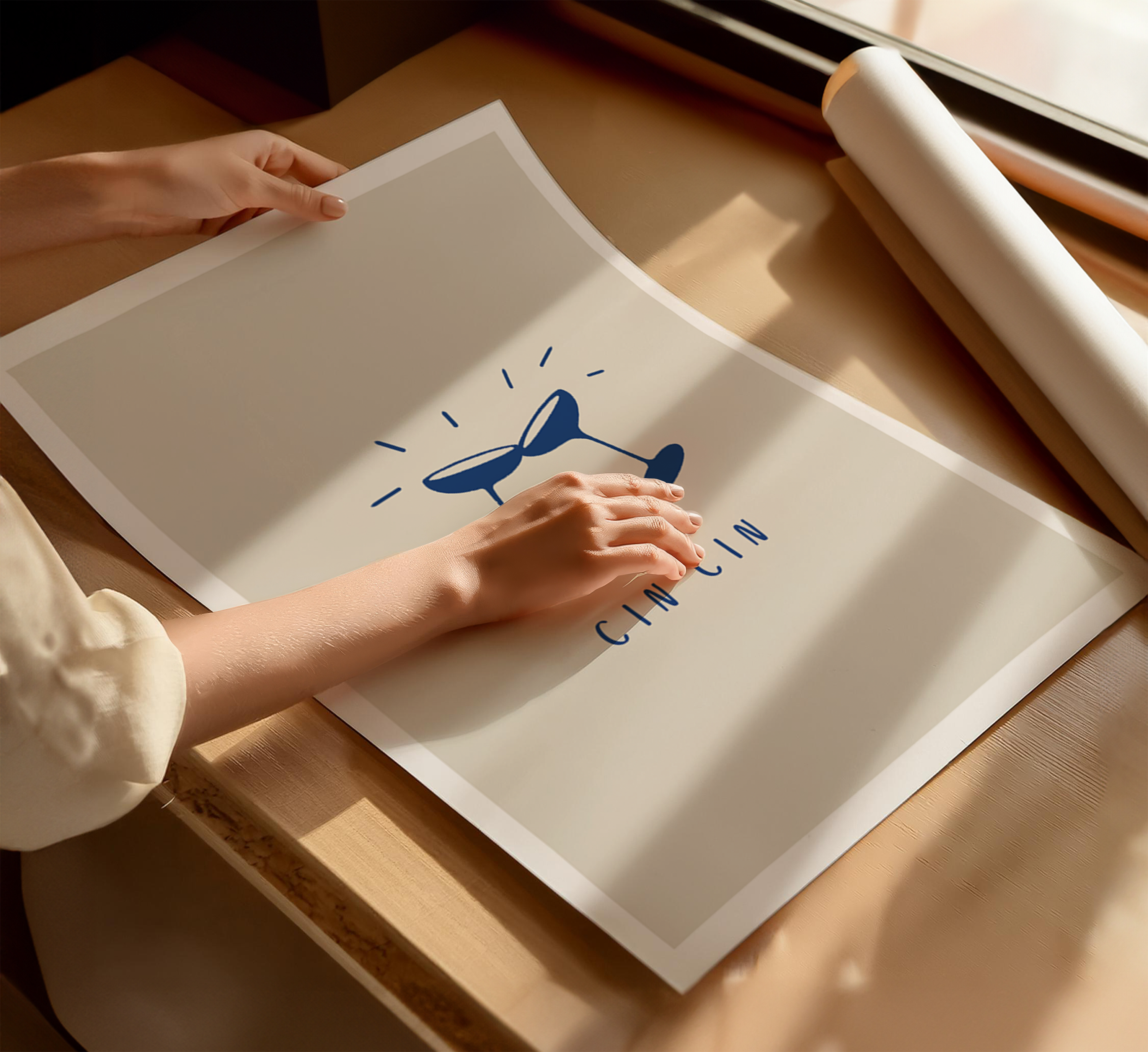 Art print featuring "cin cin" typography and illustration of two wine glasses against a beige background with white border. A person is handling the unframed print.