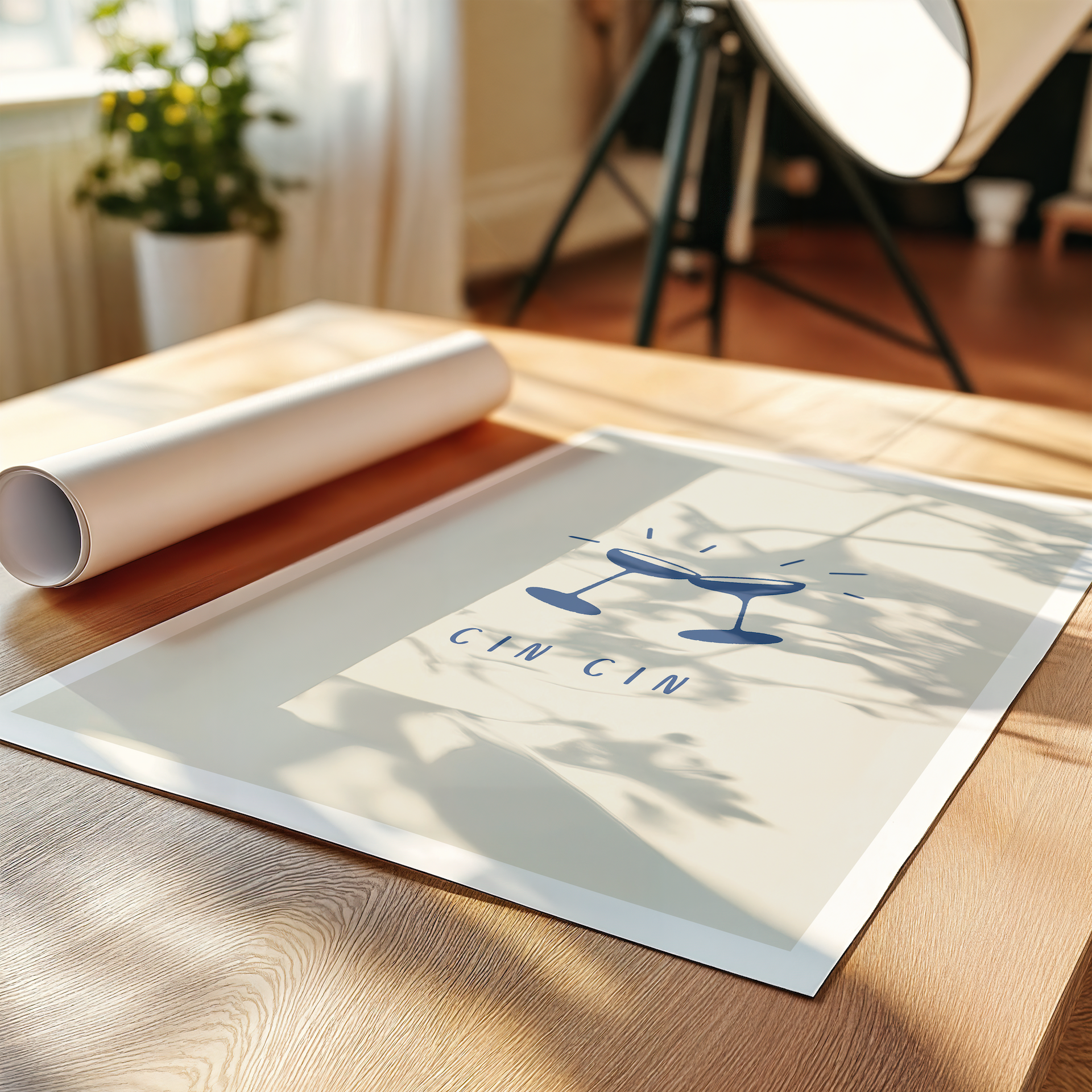 An Italian "Cin Cin" poster featuring two prosecco coupes clinking. The print lays flat on a table in a room with plant and lamp for an aesthetic look.