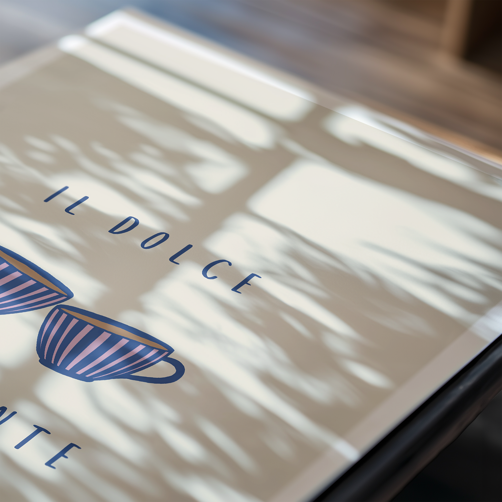 Close up image of an art print featuring typography "il dolce far niente" and illustration of two coffee cups with light shadows hitting the paper.