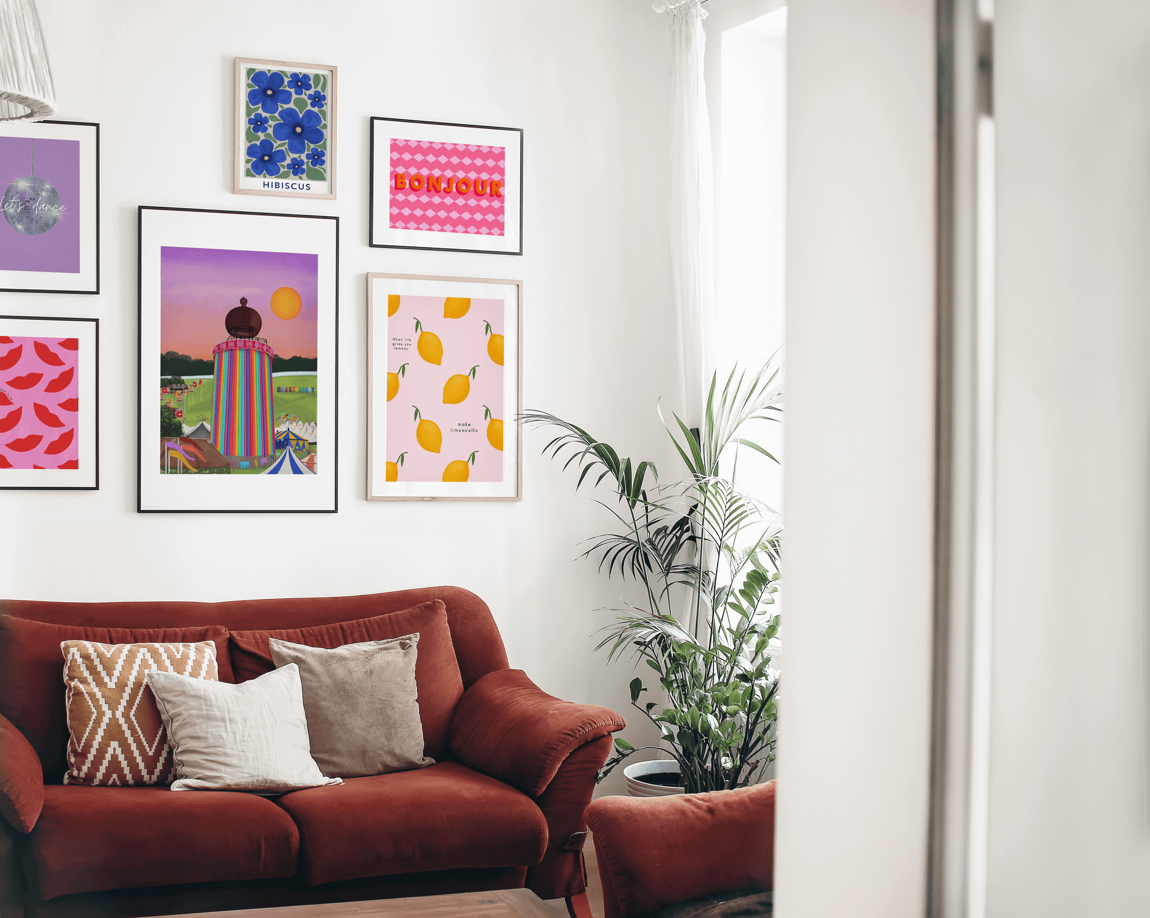 A gallery wall filled with colourful art prints in a living room with red sofa and decorative pillows and plants.