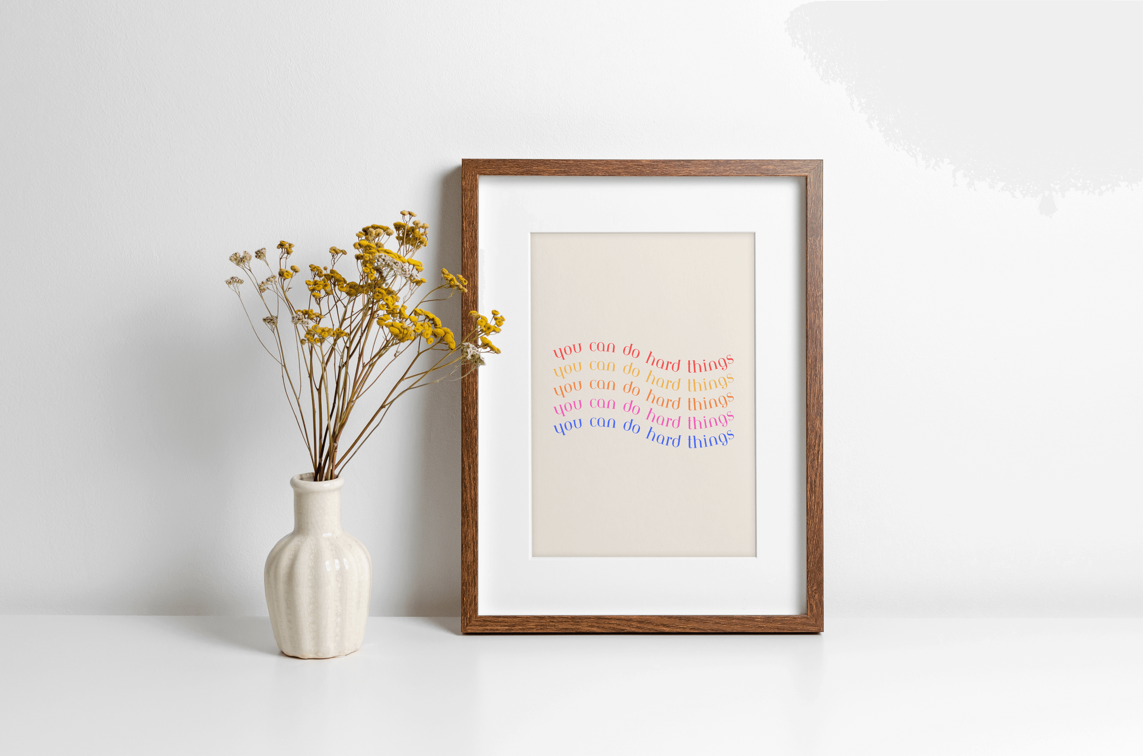 A framed art print with the phrase 'You can do hard things' in a colourful, bold typography, presented in a simple wooden frame alongside decorative vase