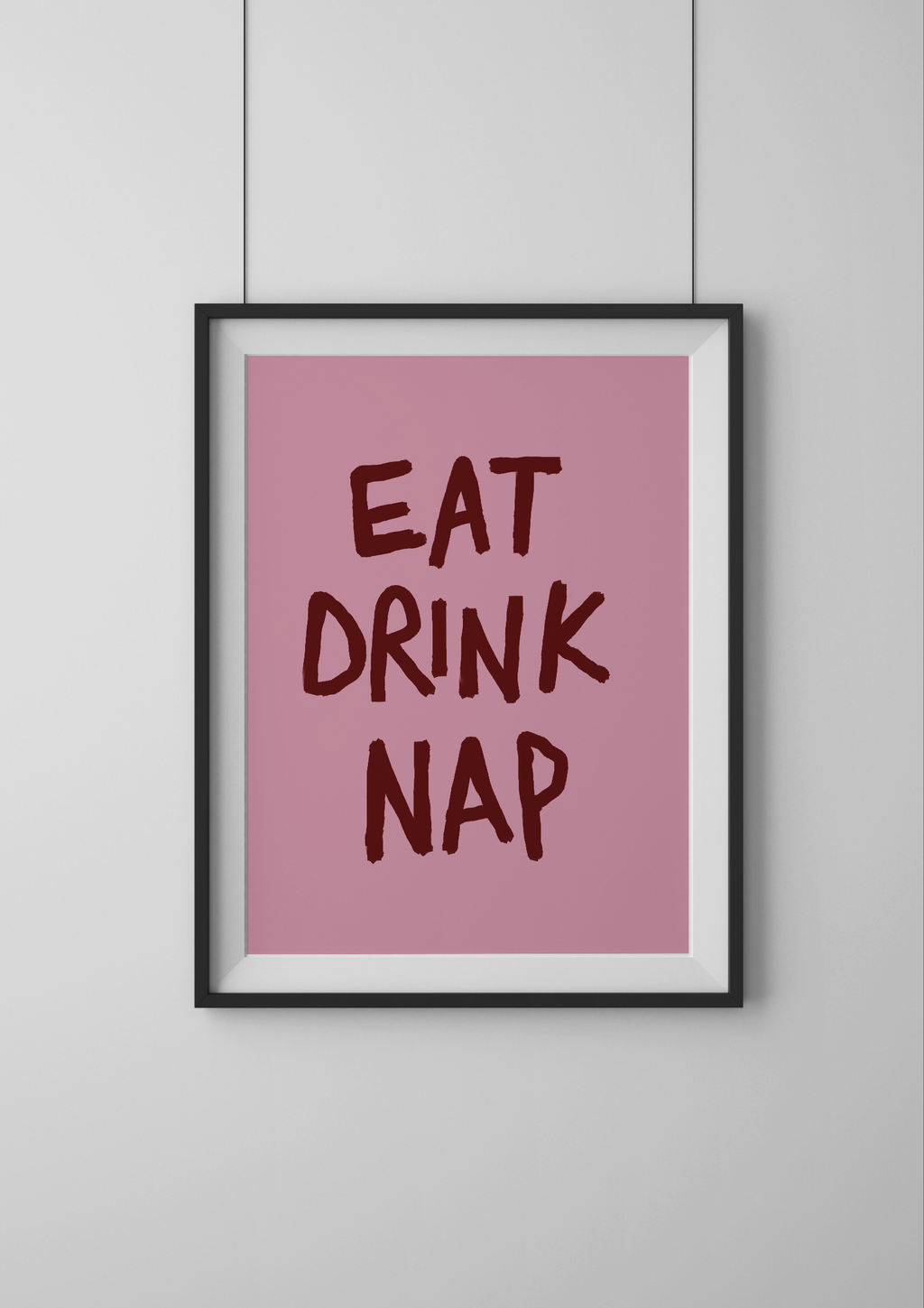 Framed poster with 'Eat Drink Nap' text on a pink background, mounted on a white wall.