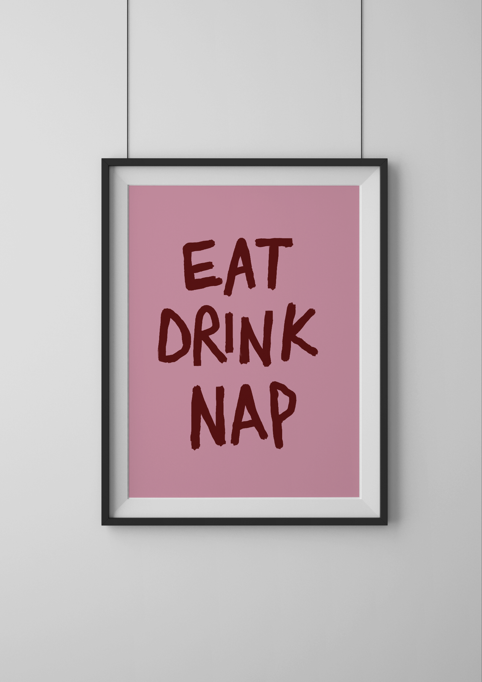 Framed poster with 'Eat Drink Nap' text on a pink background, mounted on a white wall.