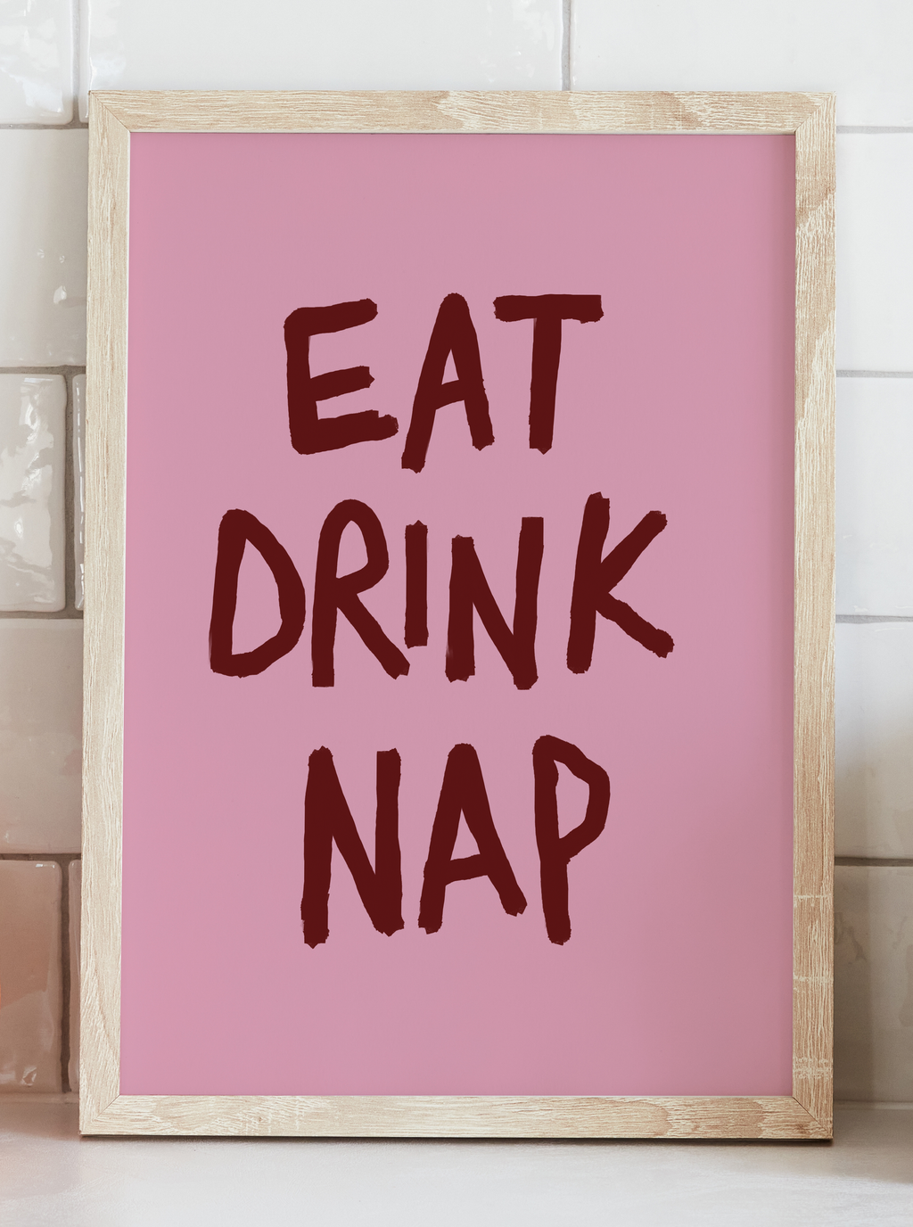 Framed pink poster with 'EAT DRINK NAP' text on a white wall.