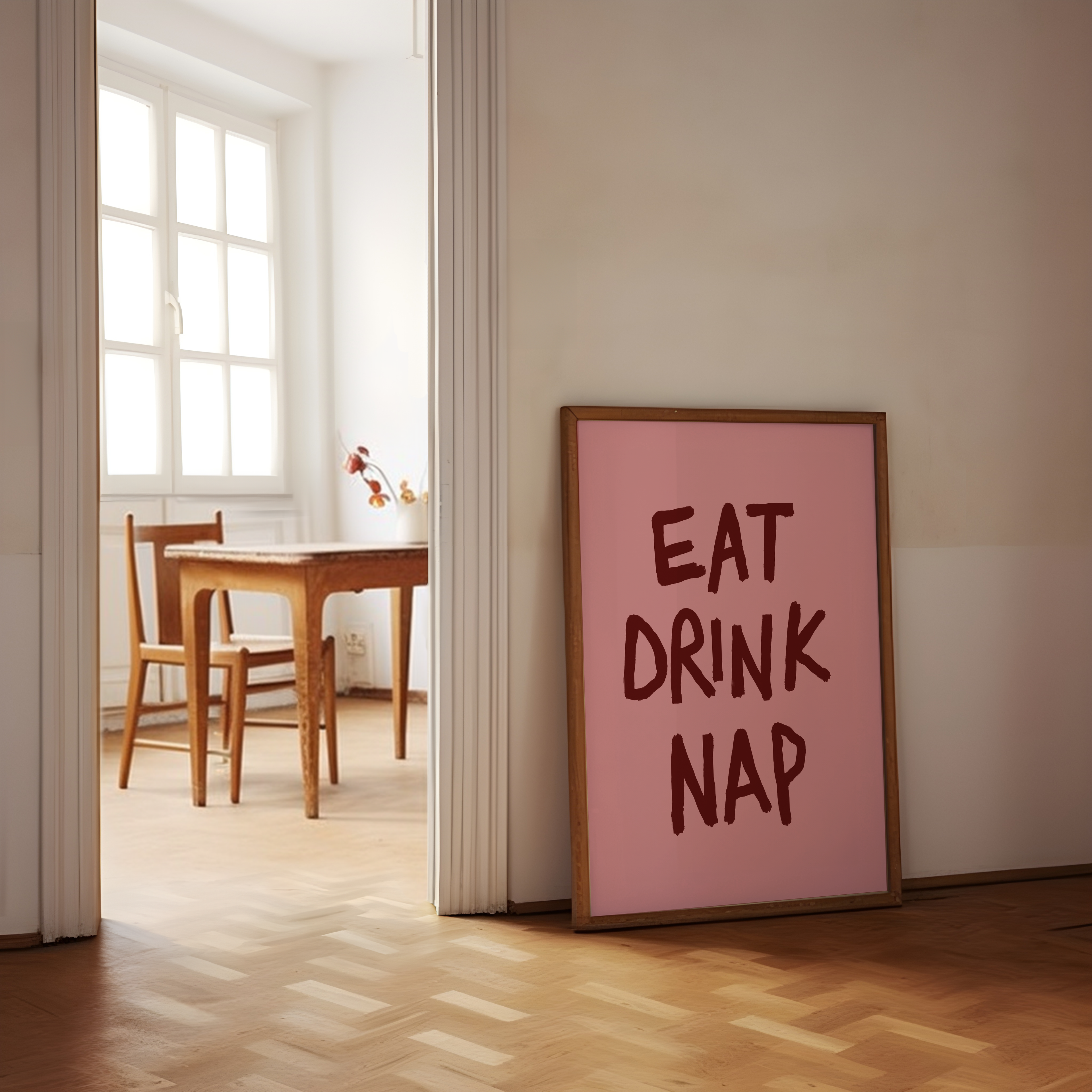 Pink framed poster with 'EAT DRINK NAP' text in a room with wooden floor and table.