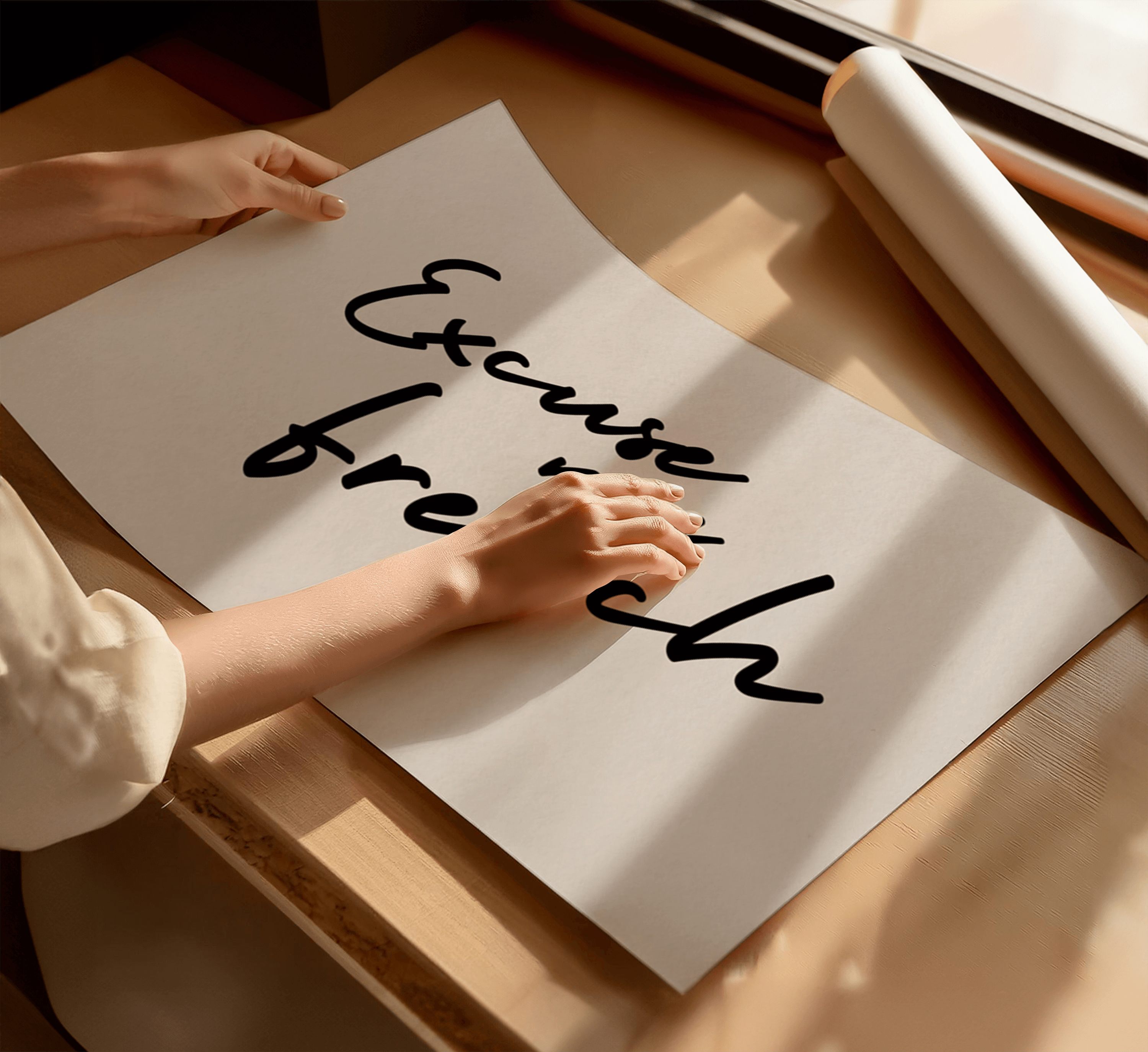 Person holding an art print with cursive text "excuse my french" on a wooden table.
