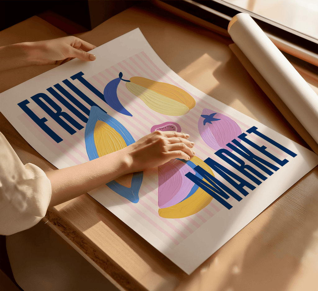 Person holding a art print with colourful fruit illustrations and text on a wooden surface.
