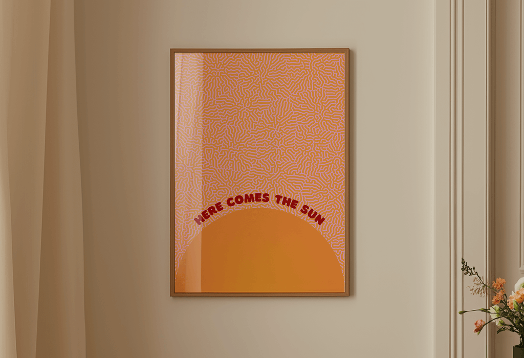 Framed abstract art print with 'Here Comes the Sun' text on a beige wall.