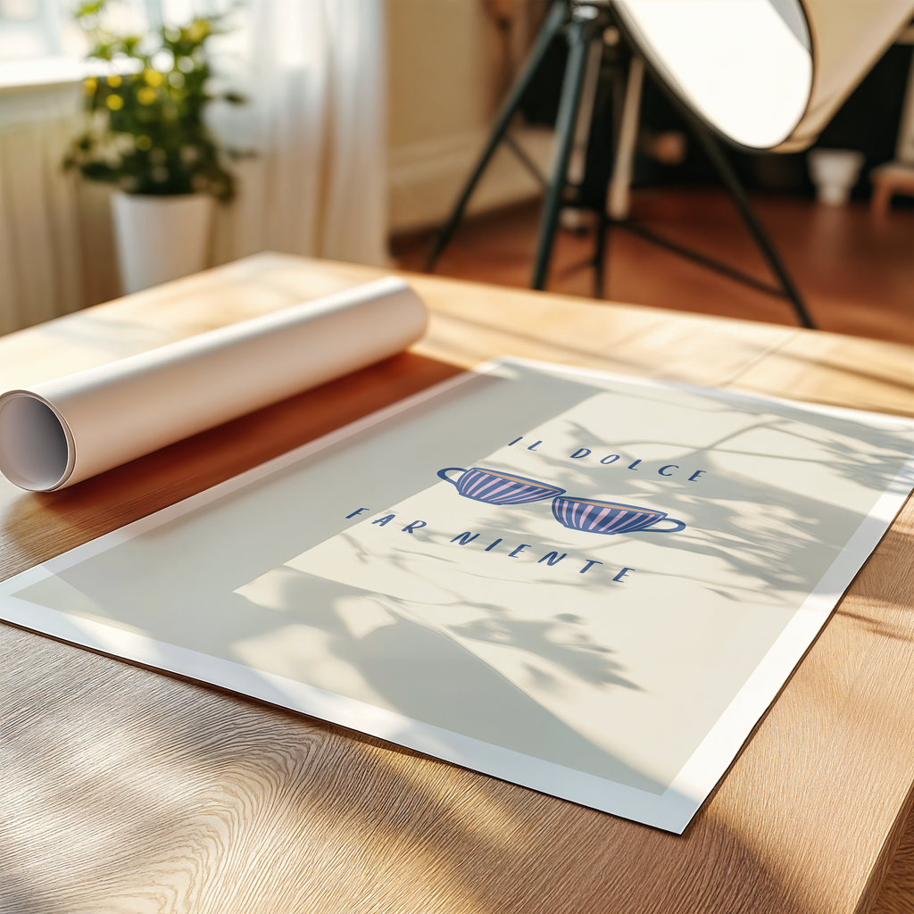 An art print laying on a table featuring Italian typography "il dolce far niente" and two coffee cups in a room with decorative plant and lamp