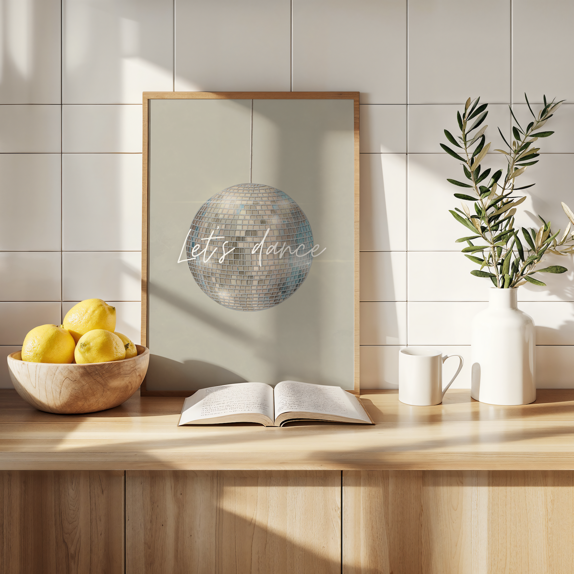 Framed artwork with 'Let's dance' text on a wooden shelf with lemons, an open book, and a plant.