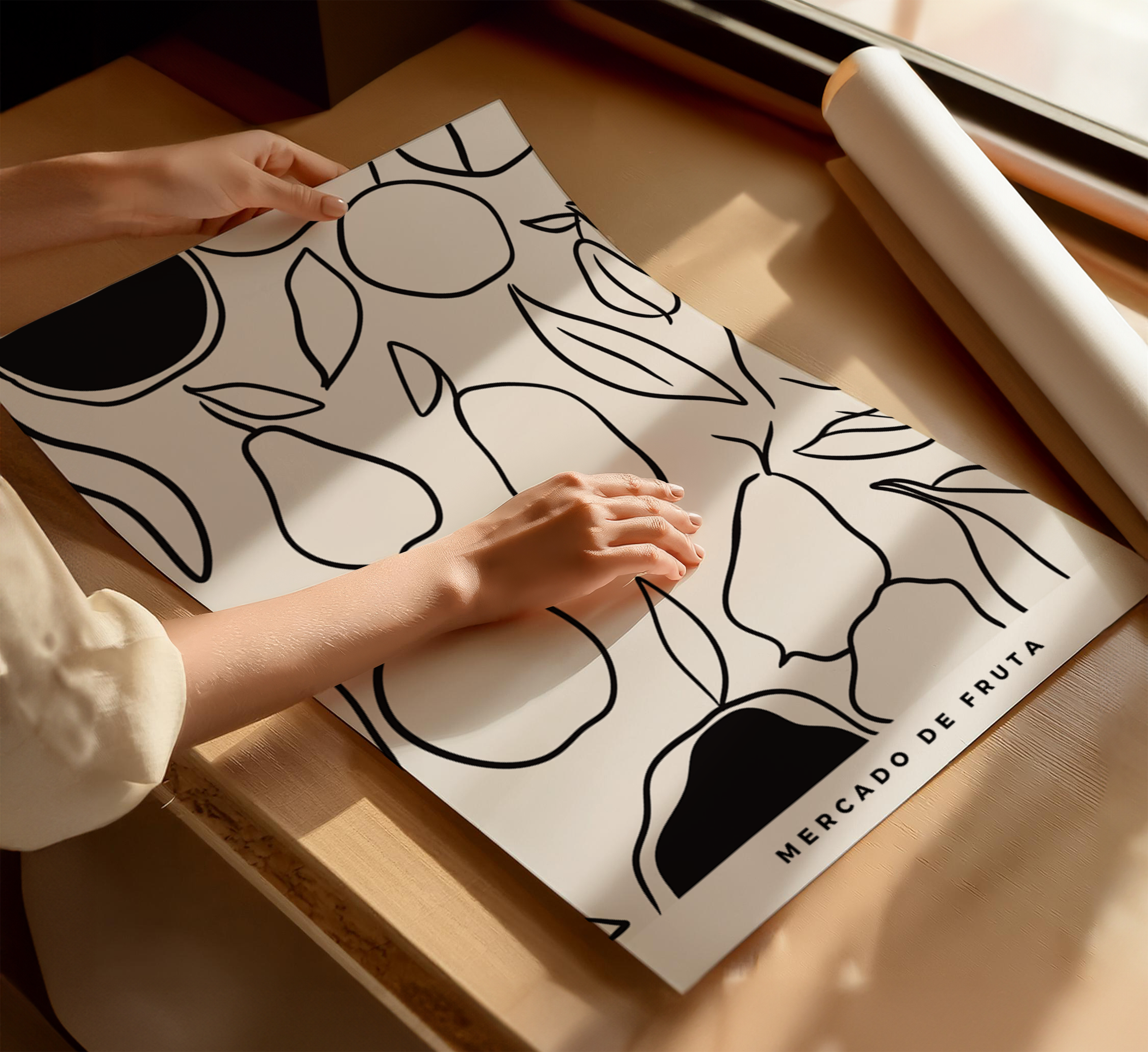 Person rolling out a white print with black fruit illustrations on a wooden surface.