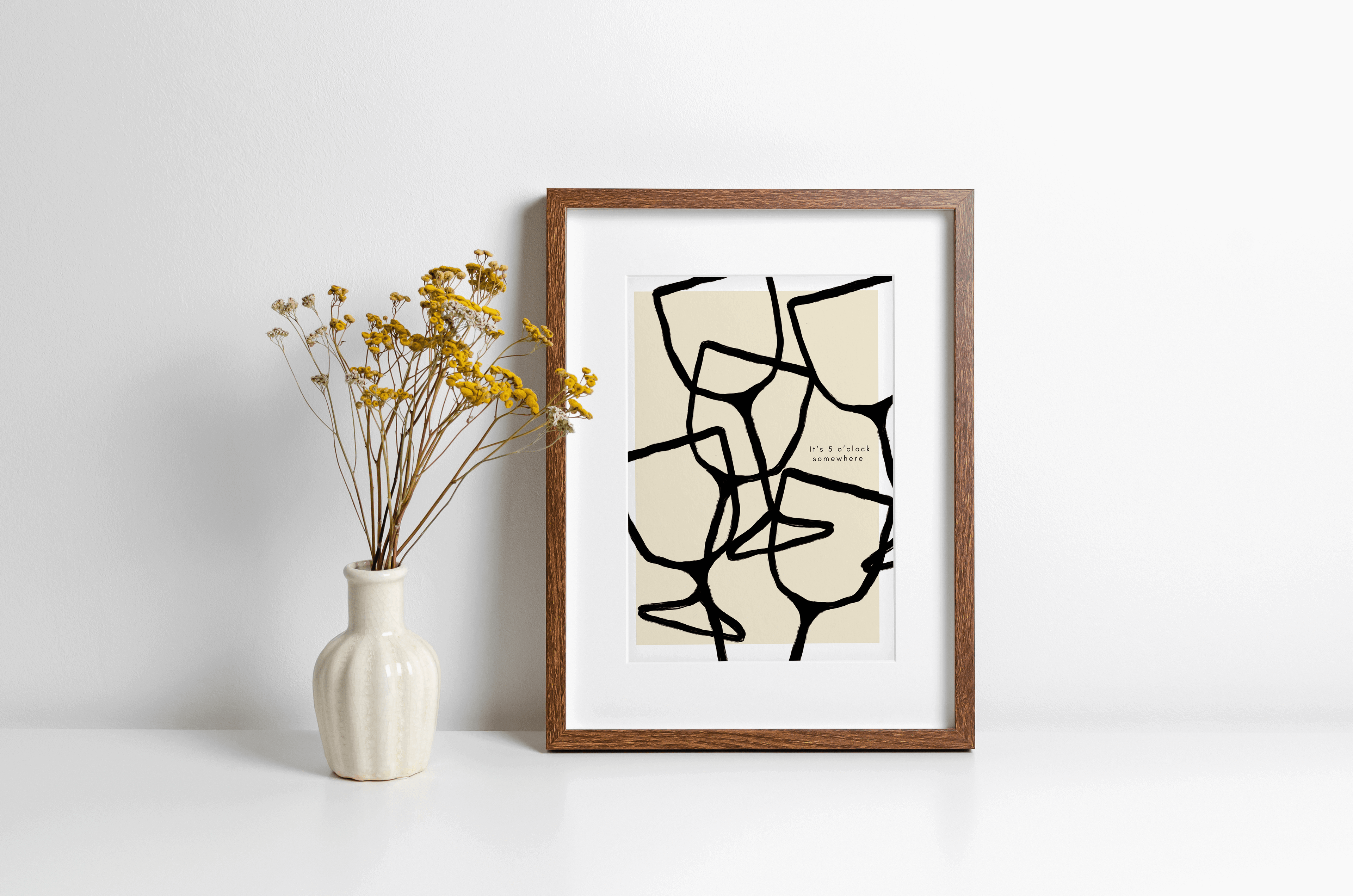 Wall art print featuring black wine pattern illustration in bold black line art and typography "it's 5 o'clock somewhere" alongside. Print is displayed in a wooden frame leaning against a wall.