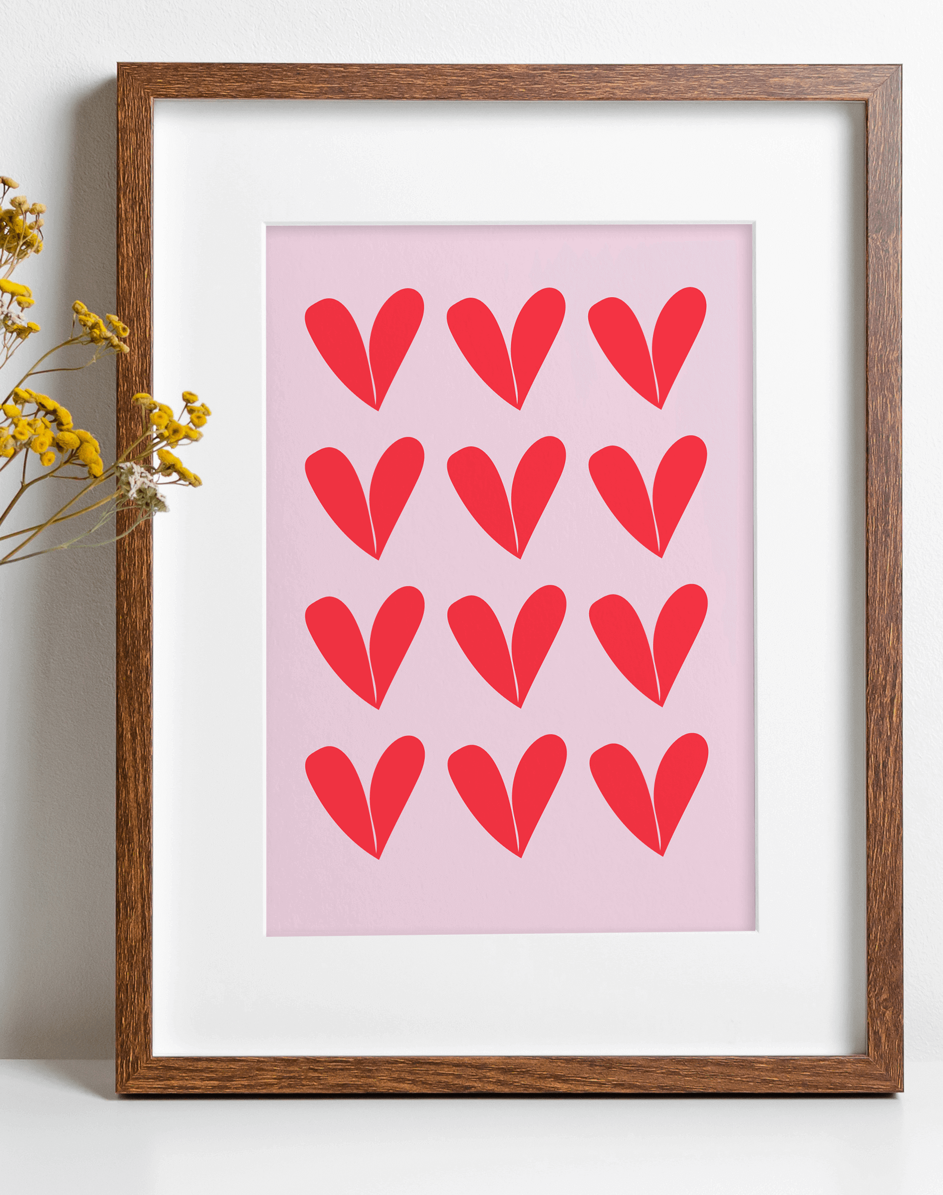 Wall art print featuring repeat heart pattern in red against a pink background, displayed in a wooden frame.