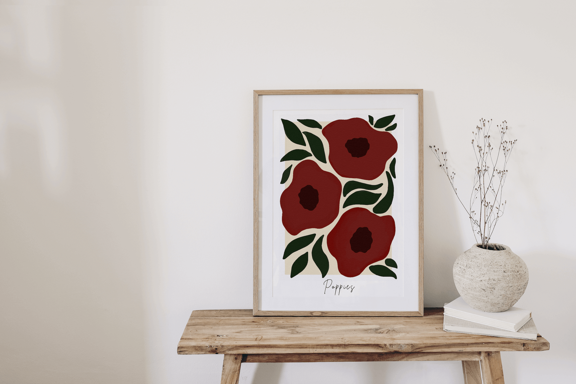 Framed artwork of red flowers on a wooden table against a white wall