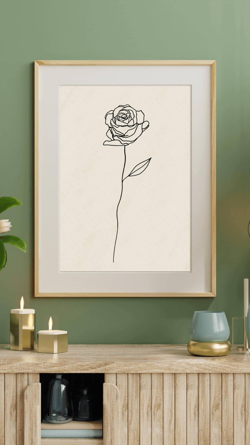 Minimalist line art print featuring a line drawing of rose, on a neutral background displayed in a wall hung frame against a green wall, above sideboard with decorative items.