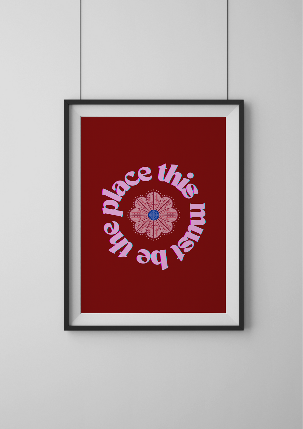 Framed artwork with a red background and pink text and flower design on a white wall.